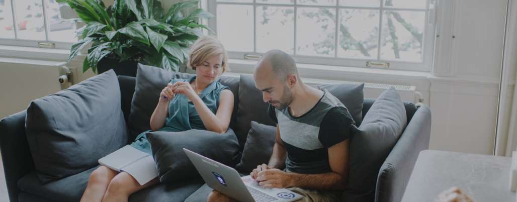 Two people sitting on a sofa working with a laptop